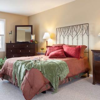 A cozy bedroom featuring a large bed with decorative pillows and a metal headboard, complemented by a dresser with a mirror and warm lighting.