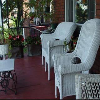 A cozy porch with wicker chairs, a small table, and lush greenery.