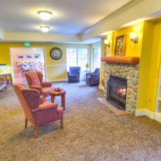 A cozy living room with armchairs facing a stone fireplace and carpeted flooring.
