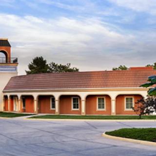 A scenic view of a building with arched architecture and a courtyard under a blue sky with clouds.