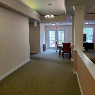 A bright hallway leading to a dining area with large windows and a carpeted floor.