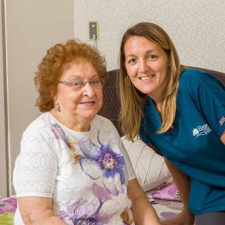 A caregiver and an elderly woman smiling together indoors.