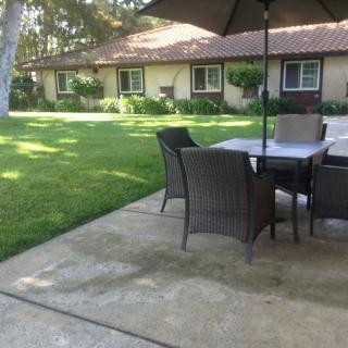 A tranquil outdoor patio setup with a table and chairs under an umbrella, located beside a lush garden.