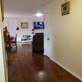 A cozy living room with a hallway, featuring hardwood floors, furniture, and a television.