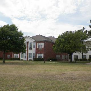 An apartment complex surrounded by green grass and trees under a cloudy sky.