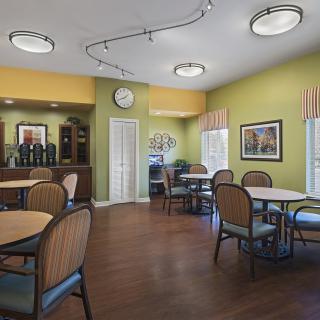 A cozy dining area with multiple tables and chairs, featuring green walls and wooden flooring.