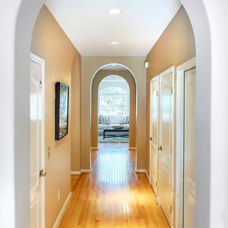 A well-lit hallway with an archway and wooden flooring, featuring neutral-colored walls and doors on either side.