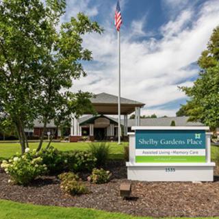Front view of a building with landscaped garden and a sign at the entrance under a cloudy sky.