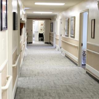 An empty hallway in a healthcare facility, featuring neutral-colored walls and bright lighting.