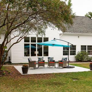 A cozy backyard patio area featuring outdoor furniture and a bright blue umbrella, surrounded by well-maintained landscaping.