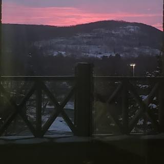 A serene winter sunset over the mountains, framed by a rustic railing.