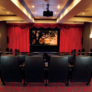A luxurious home theater with rows of seats facing a large movie screen, framed by red curtains.