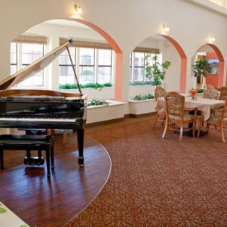 A spacious and elegant room featuring a grand piano and a dining area with arched windows.