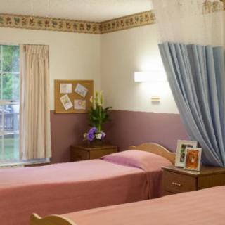 A cozy bedroom with twin beds, floral decor, and soft curtains by a window.