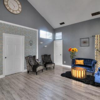 A modern living room with gray walls, featuring a blue sofa, accent chairs, sunflowers in a vase, and stylish decor.