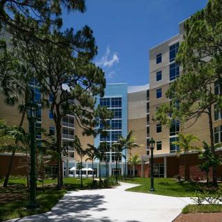 A modern university campus building surrounded by trees and a clear blue sky.