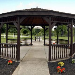 A wooden gazebo situated in a landscaped park with surrounding greenery and fences.