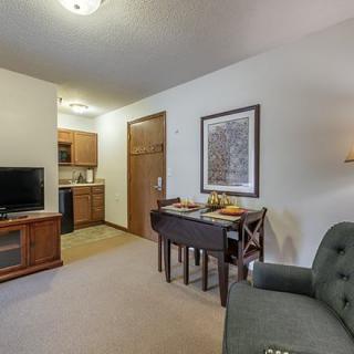 A cozy apartment living space featuring a small dining table, a television, and an open kitchen.