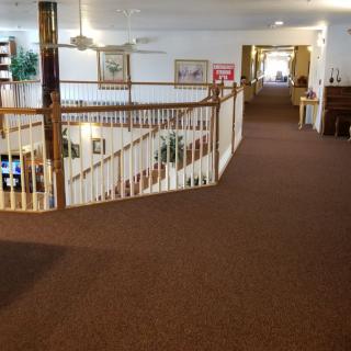 A spacious hallway with railings overlooking a staircase, featuring carpeted floors and decorative elements.