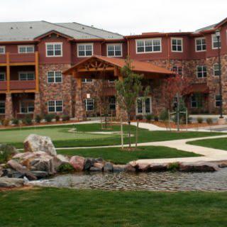 A view of a residential building with well-maintained gardens and a small pond.