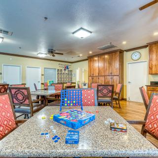 A spacious community room with tables and chairs arranged for leisure activities, featuring a Connect Four game set up on one of the tables.