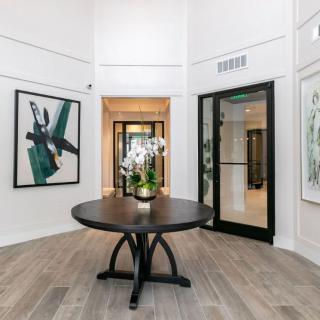 A modern foyer featuring a round table with flowers, surrounded by contemporary artwork and leading into a hallway.