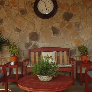 An inviting patio with wooden furniture, lush plants, and a decorative clock on a stone wall.