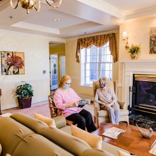 Two seniors sitting in a cozy living room with a fireplace and natural light.