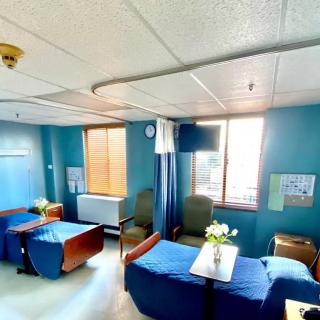 A hospital room with patient beds, chairs, and windows letting in natural light.