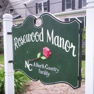 A green sign for Rosewood Manor, featuring a rose and indicating it as a North Country facility.