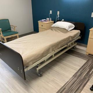 A hospital room featuring a patient bed, bedside tables, and a chair.