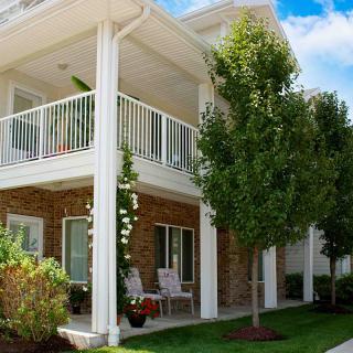 A modern house with a balcony and porch, surrounded by a garden and trees.