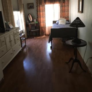 A cozy room with a bed, dresser, table, and lamp near a window with curtains.
