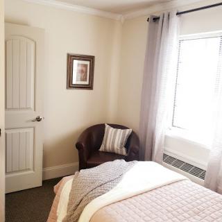 A cozy and well-lit bedroom featuring a comfortable bed, a stylish chair, and decorative artwork.