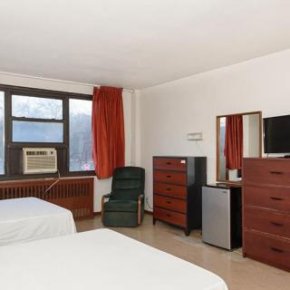 A hotel room with two beds, an air conditioner, and various pieces of furniture including a dresser and television.