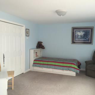 A simple bedroom with a single bed, blue walls, and a cozy chair.