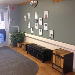 A cozy waiting area featuring a green wall adorned with framed photographs, complemented by wooden seating and a decorative plant.