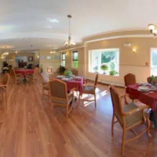 A spacious dining area with several tables and chairs, featuring large windows and warm lighting.