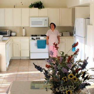 A person stands in a bright kitchen with flowers on the table.