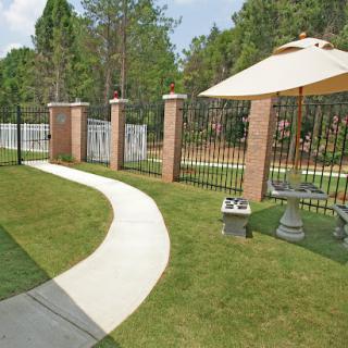 A serene pathway leading through a well-maintained garden with a fence and sunshade.