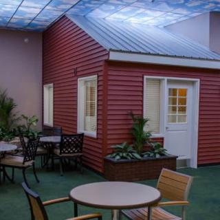 An indoor space featuring a seating area with tables and chairs, adjacent to an artificial red house facade with plants.