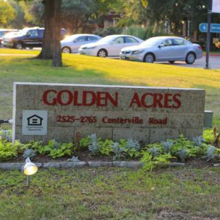 A sign for Golden Acres with cars parked in the background.