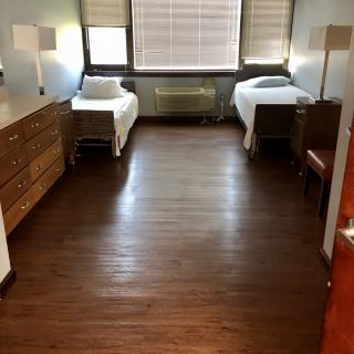 A minimalist dorm room with twin beds, wooden flooring, and simple furnishings.
