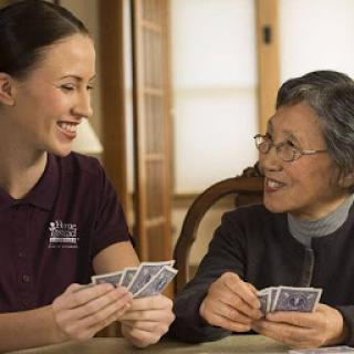 A caregiver and an elderly woman enjoying a friendly card game together, sharing smiles and conversation.