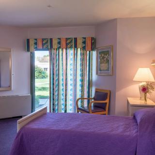 A cozy bedroom with a purple bedspread, a chair, and stylish curtains letting in natural light.