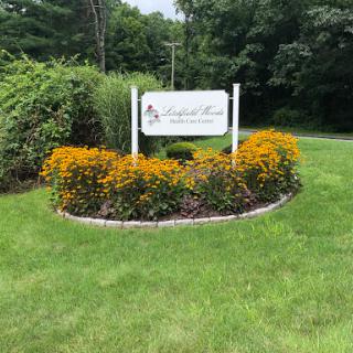 A welcoming sign surrounded by vibrant flowers and lush green grass.