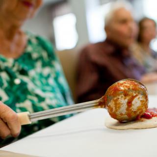 An elderly person participates in a social activity involving food preparation or enjoyment.