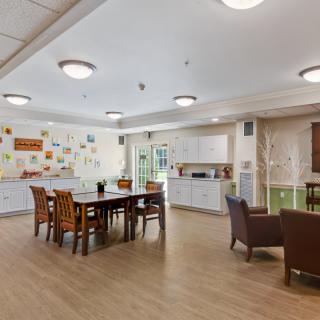 A spacious community dining area with a kitchen, featuring tables and chairs, adorned with colorful wall decorations.