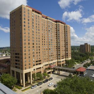 A view of a modern high-rise residential building against a blue sky with scattered clouds.