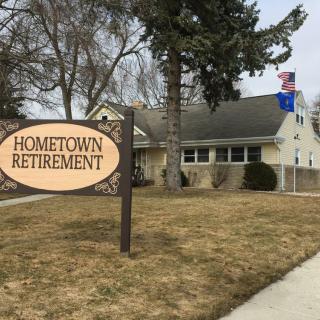 Sign for Hometown Retirement in front of a residential building with a flag and trees.